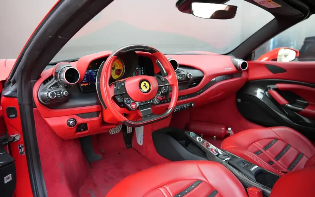 Interior view of a Ferrari convertible featuring eye-catching seats, a dashboard, and floor mats in bright red leather, complemented by carbon-fiber accents. Why Car Rental Abu Dhabi Monthly Is the Smartest Choice for Expats, Professionals, and Long-Term Visitors