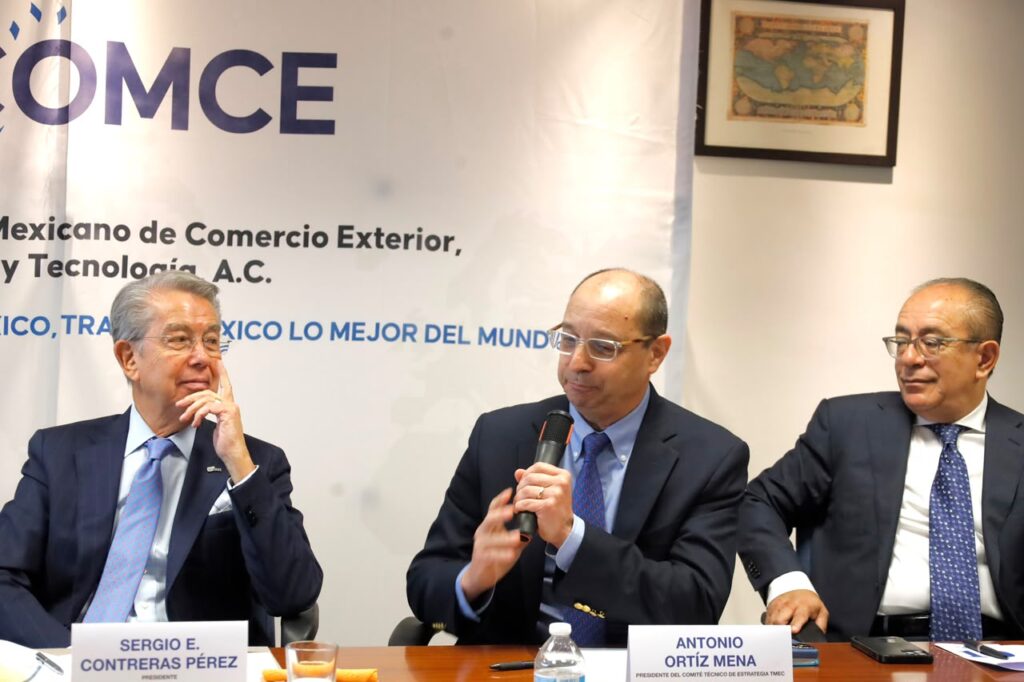 Antonio Ortiz-Mena on the podium during a press conference in Mexico City, speaking in front of microphones and screens, with a COMCE institutional banner and attendees taking notes.