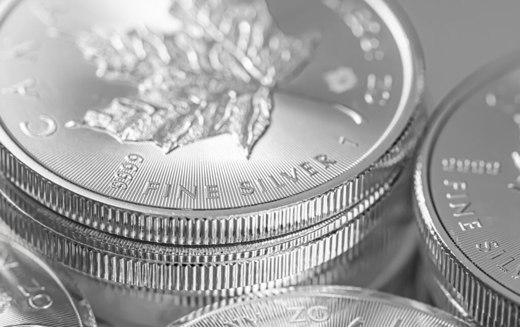A black-and-white close-up showing a stack of silver bullion coins, with the inscription “FINE SILVER” and a raised Canadian maple leaf design visible on the top coin.