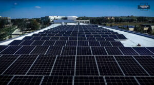 Vista aérea detallada de un extenso arreglo de paneles solares instalados sobre el techo plano y blanco de un moderno edificio comercial, mostrando eficiencia energética bajo un cielo despejado.