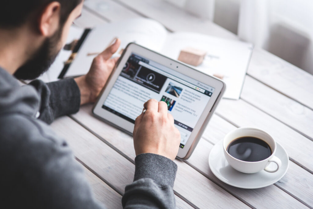 Profesional revisando portales de noticias digitales y notas de prensa en una tableta sobre su escritorio de trabajo, evaluando métricas y cobertura mediática para campañas de PR y SEO.