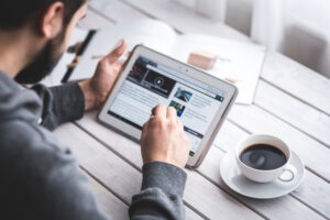 Profesional revisando portales de noticias digitales y notas de prensa en una tableta sobre su escritorio de trabajo, evaluando métricas y cobertura mediática para campañas de PR y SEO.