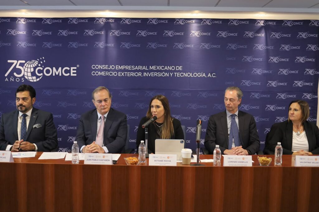 Betsabé Rocha fala ao microfone em um pódio da COMCE, ladeada por empresários, anunciando o Congresso de Comércio Exterior e a importância da rodovia La Gloria-Colômbia.
