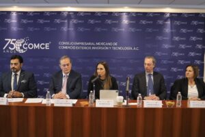 Betsabé Rocha habla en un micrófono en un presídium de COMCE flanqueada por empresarios, anunciando el Congreso de Comercio Exterior y la relevancia de la carretera La Gloria-Colombia.
