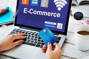 Persona escribiendo credenciales en una laptop que muestra una interfaz de inicio de sesión de comercio electrónico con la palabra "E-Commerce", sosteniendo una tarjeta de crédito "PREMIUM Credit" sobre un escritorio de madera.