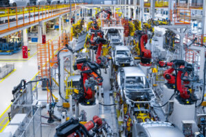 A highly automated automotive assembly line with multiple red industrial robotic arms working on vehicle bodies inside a modern manufacturing plant in North America.