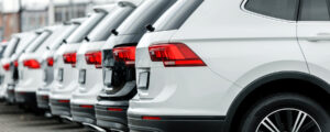Línea de camionetas SUV modernas de color blanco y gris estacionadas en fila, mostrando la parte trasera y sus calaveras rojas en un lote de autos nuevos y seminuevos. ¿Conviene usar el dinero de la venta de tu auto como enganche para comprar otro?