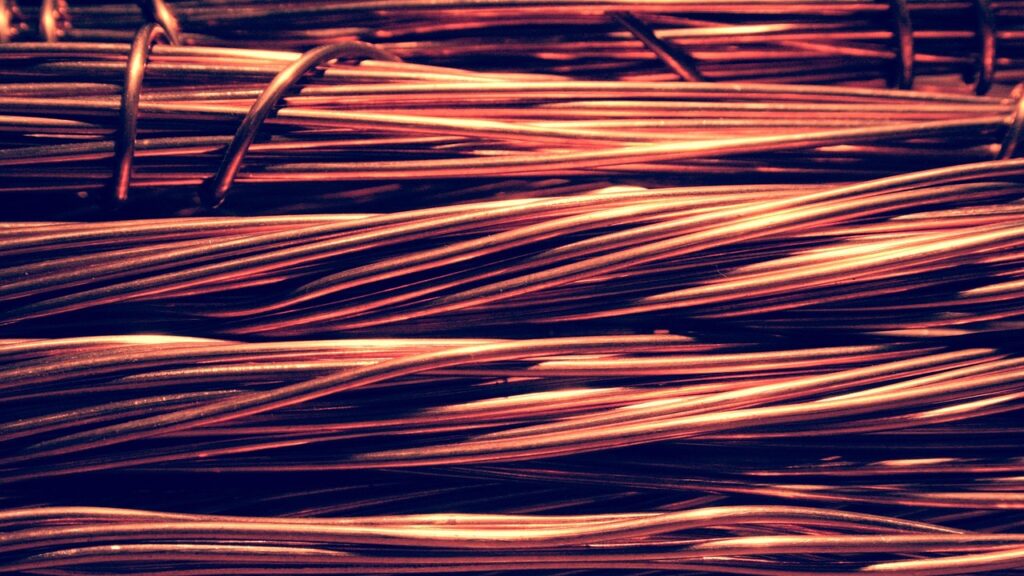 Primer plano detallado de gruesos hilos y cables de cobre enrollados industrialmente con destellos metálicos rojizos, representando la producción, exportación y fuerza del sector minero en la economía chilena.